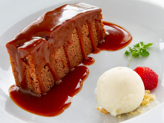 Plate with a slice of sticky tofee pudding, toffee sauce on top and a scoop of vanilla ice cream.