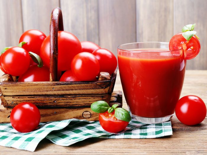 A glass filled with tomato juice kept next to a basket of fresh tomatoes