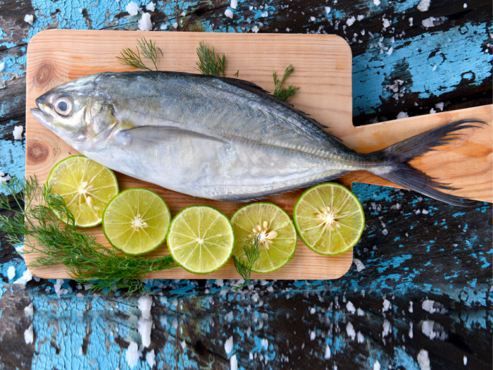 Flatline picture of trevally fish placed on a wooden board with lime halves and sprigs of dill.