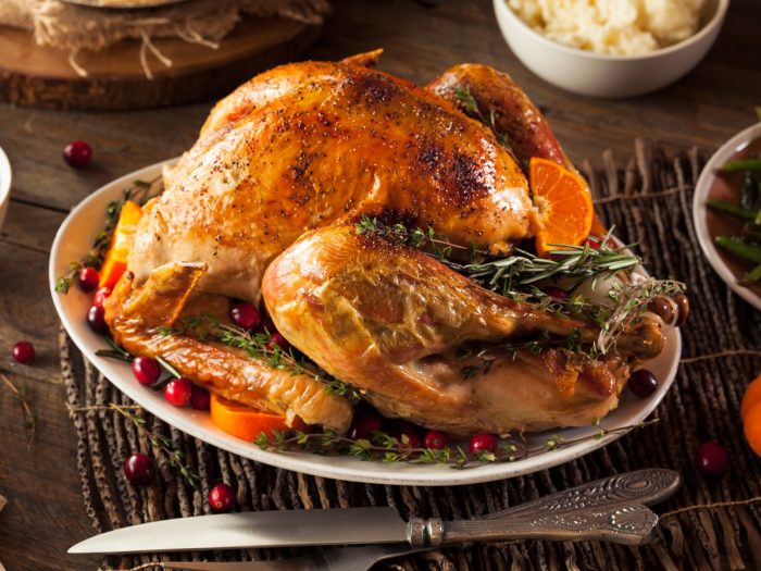 Roast turkey on a plate on a wooden table next to mashed potatoes and a carving knife