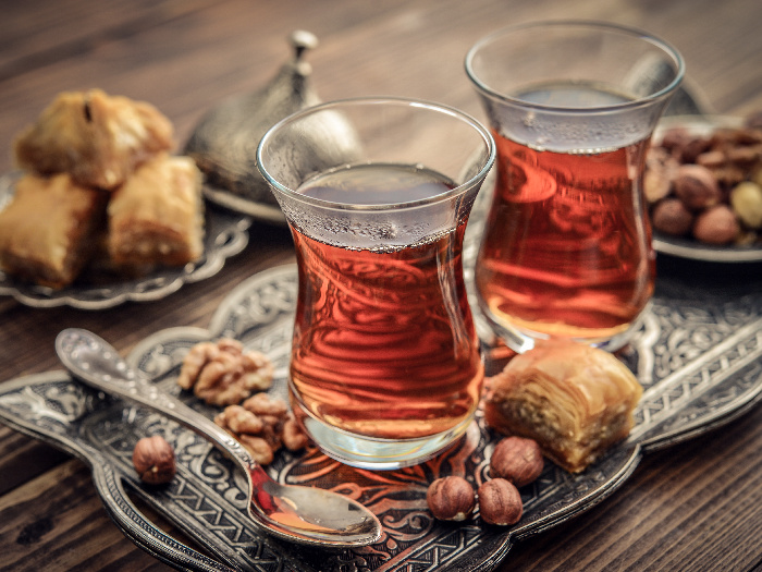 A cup of Turkish tea served in traditional style with baklava and nuts in the background