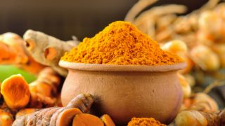 Fresh turmeric and a bowl and a spoon with turmeric powder