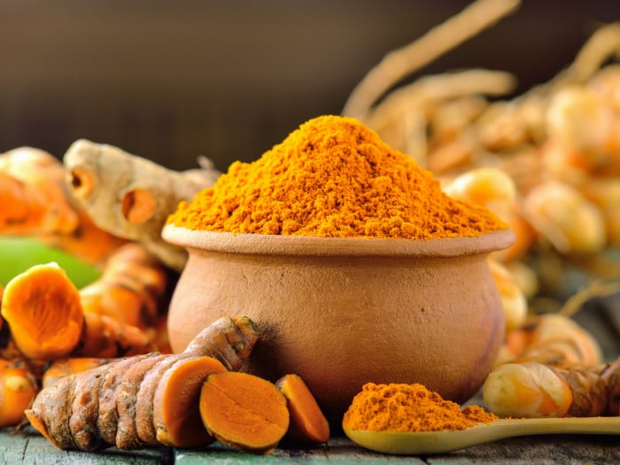 Fresh turmeric and a bowl and a spoon with turmeric powder