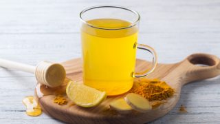A close up shot of turmeric ginger tea, made with turmeric, ginger, lemon and honey on a wooden board