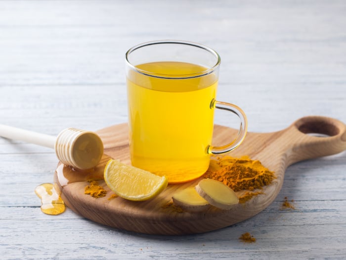 A close up shot of turmeric ginger tea, made with turmeric, ginger, lemon and honey on a wooden board