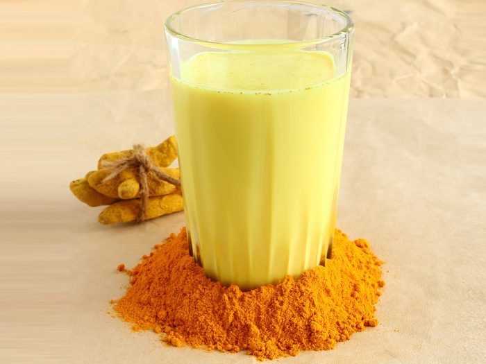 A glass filled with turmeric milk, surrounded by turmeric powder around its surface