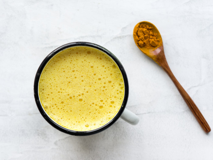 A cup filled with turmeric milk kept next to a spoonful of turmeric powder