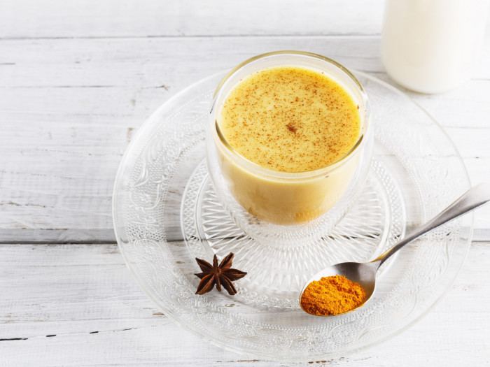 A spoonful of turmeric and star anise on a saucer and a cup of turmeric tea.