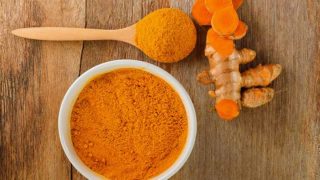 Raw turmeric root and turmeric powder in a bowl and spoon on wood
