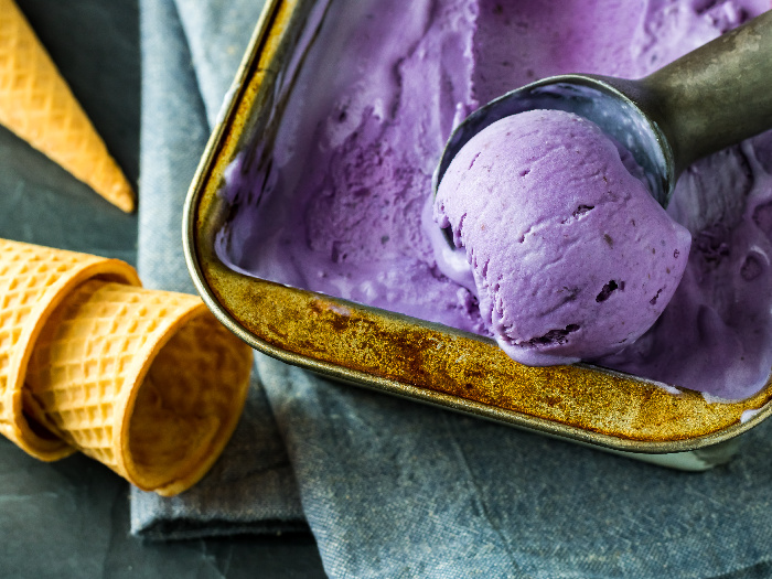 Ube ice cream being scooped out of a bowl next to ice cream cones