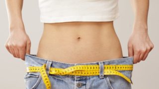 A woman holding a pair of large jeans around her waist to show how much weight she has lost