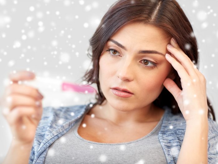 A woman holding a pregnancy test and looking worried