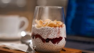 A delicious glass of vanilla chia pudding garnished with fresh fruits, kept atop a wooden slab, next to a spoon
