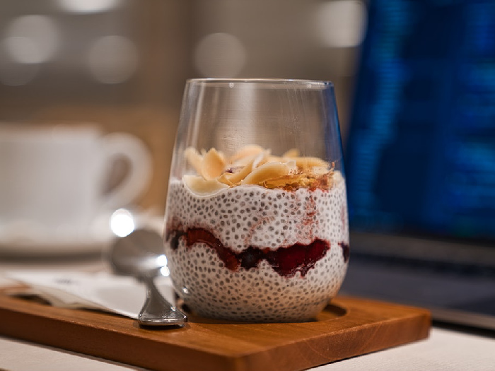 A delicious glass of vanilla chia pudding garnished with fresh fruits, kept atop a wooden slab, next to a spoon