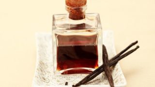 A jar of vanilla oil with dried vanilla beans on a small white tray