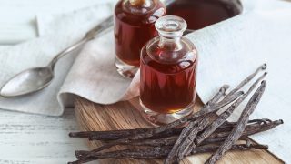 Two vanilla extract bottles next to fresh vanilla beans and a bowl of vanilla extract with a spoon
