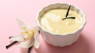 Vanilla Pudding in a white bowl kept atop a pink table, next to a white flower