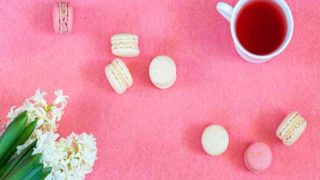 Vanilla tea in a teacup with macaroons and flowers on a pink background