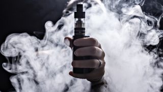 Hand holding an e-cigarette in a cloud of smoke