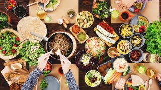 Top view of people enjoying vegetarian foods like hummus, salads, and bread