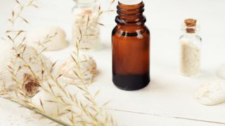 A bottle of vetiver oil with vetiver grass and small containers of sea salt on a white background