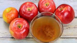 A glass full of vinegar mother surrounded by apples