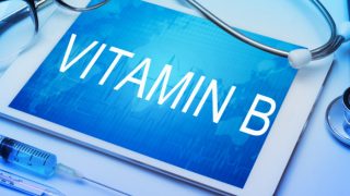 VITAMIN B' written on a tab surrounded by a stethoscope, injection, and glasses, placed on a blue surface.