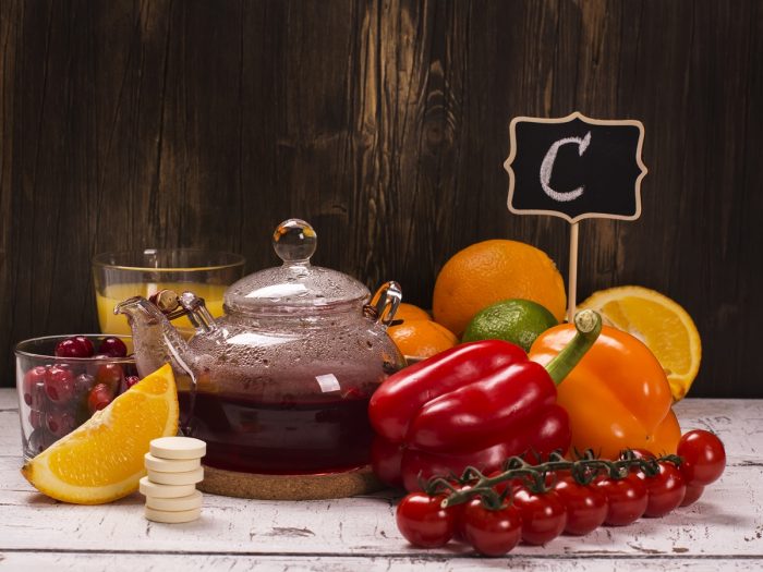 Foods rich in vitamin C (whole and halved sweet limes, red and yellow chili pepper, red cherries) with glasses of sweet lime juice and cherries on a wooden table