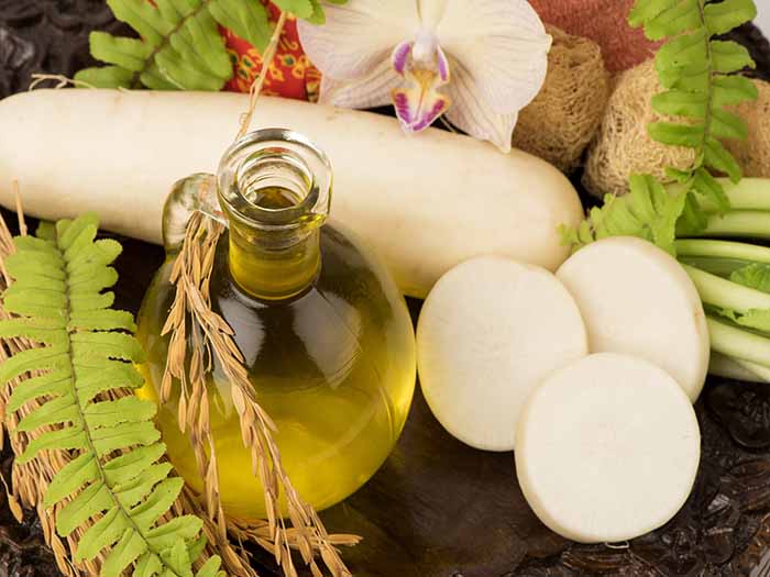 Vitamin E oil in a glass tumbler along with fresh herbs and sliced radish