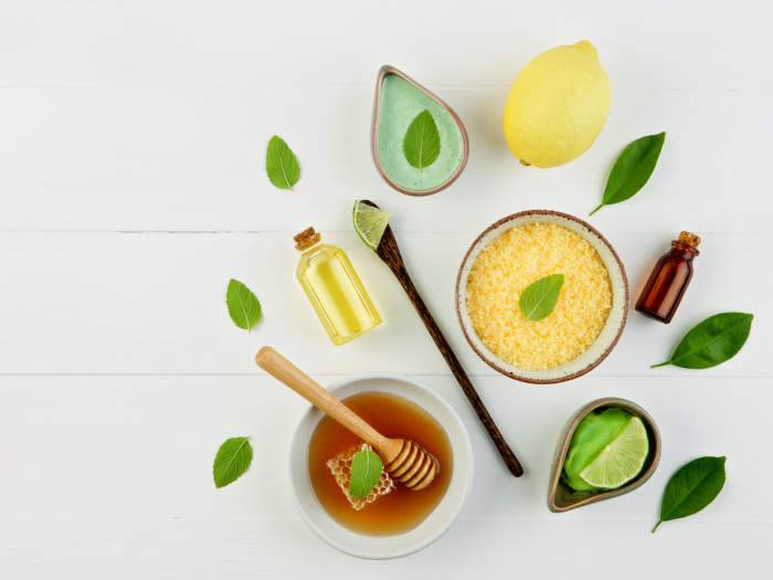 Flatline view of small bottles, spoon, leaves, bowls of honey, limes, cereal, and water