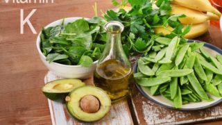Foods rich in vitamin K (spinach, peas, cilantro, bananas, olive oil, and halved avocado) on a wooden table