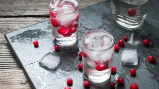 Glasses filled with vodka, ice, and cranberries kept on a black slab