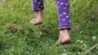 Back view of a child's legs walking on a grassy ground.