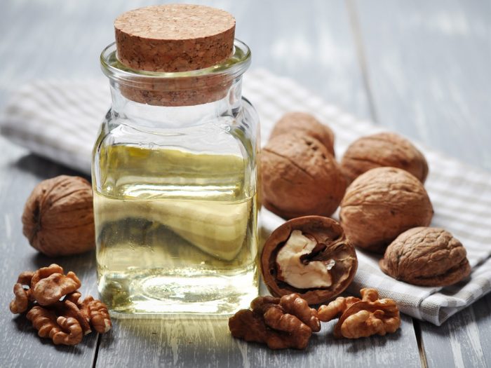 A close-up shot of walnut oil in a bottle surrounded by walnuts