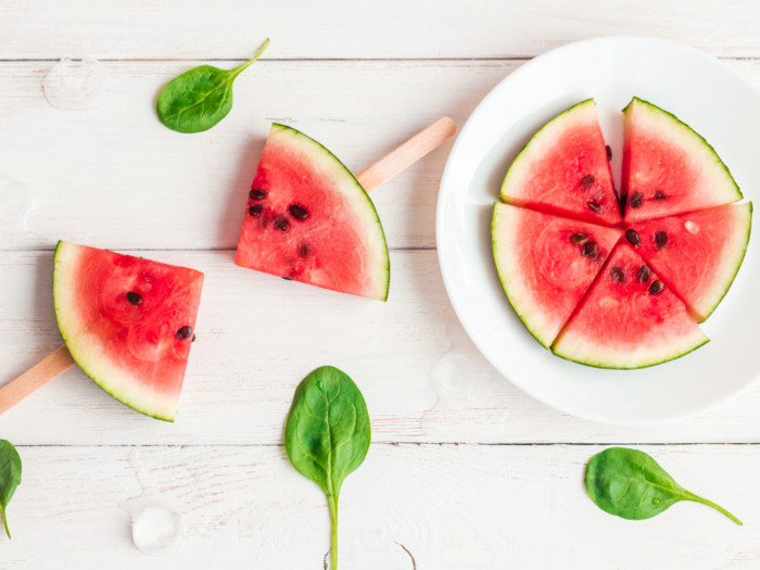 2 watermelon popsicles and a plate full of sliced watermelon on a white wooden background