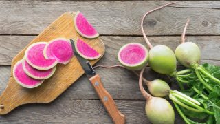 Sliced watermelon radish (Chinese daikon) with green leaves on a wooden table.