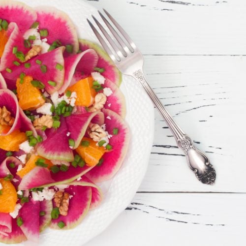 Watermelon radish, orange, and goat cheese salad on a white plate