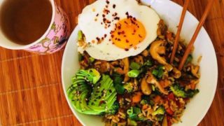 Stir-fried vegetables sauteed with rice, served with avocado and eggs to the side, placed atop a wooden table