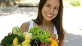 A woman smiling and holding a grocery bag of fresh fruits and vegetables