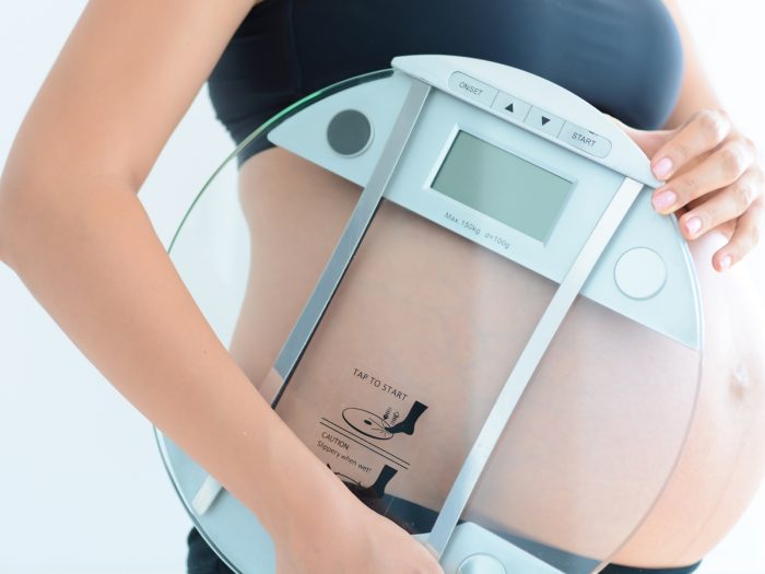 A close-up shot of a pregnant woman holding a weighing scale