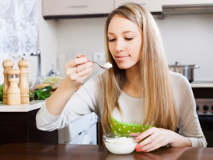 A young woman eating cottage cheese with a spoon in the kitchen