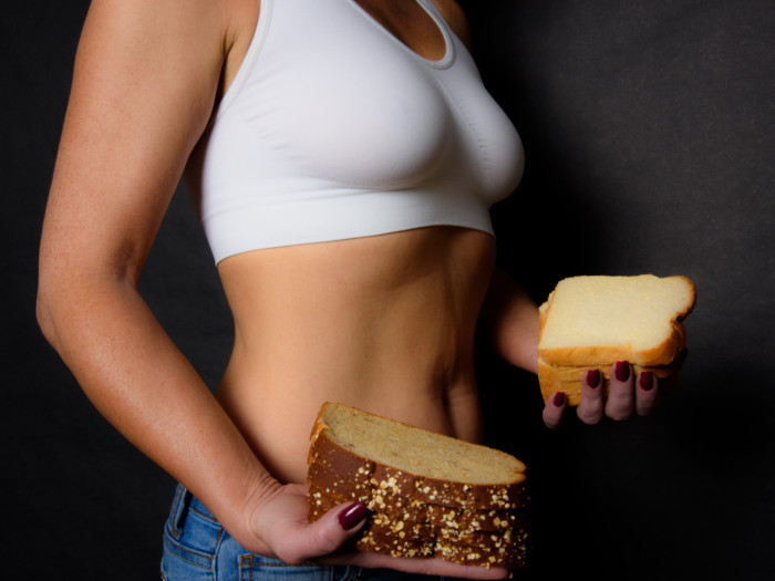 A young woman with flat tummy holding white and wheat bread - wheat belly diet