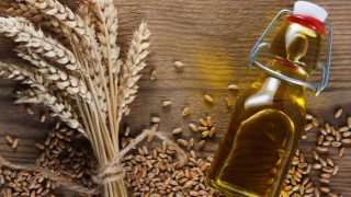 A bottle of wheat germ oil with ears of wheat and grains scattered all over the wooden table