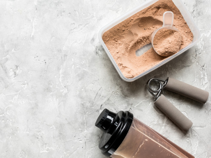 Whey protein powder, a bottle and hand press on white grey background