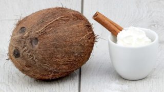 Whole coconut with a cup of whipped cream and cinnamon on a white wooden table