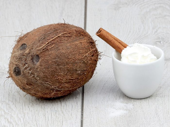 Whole coconut with a cup of whipped cream and cinnamon on a white wooden table