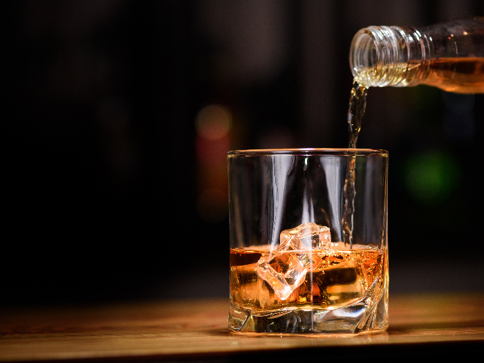 Whiskey being poured into a whiskey glass with ice cubes in it