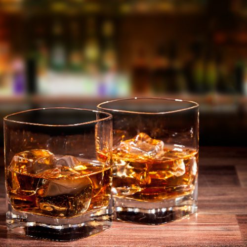 Two glasses of whiskey and ice on a wooden counter