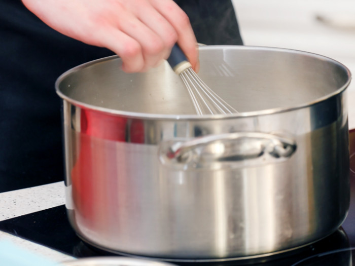 Close-up of someone using a whisk in a pan placed on a hob.