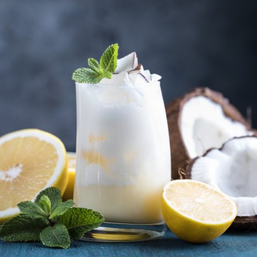 Cocktail drink with pineapple juice, coconut, grapefruit, and lemon and mint in a glass on a blue wooden background